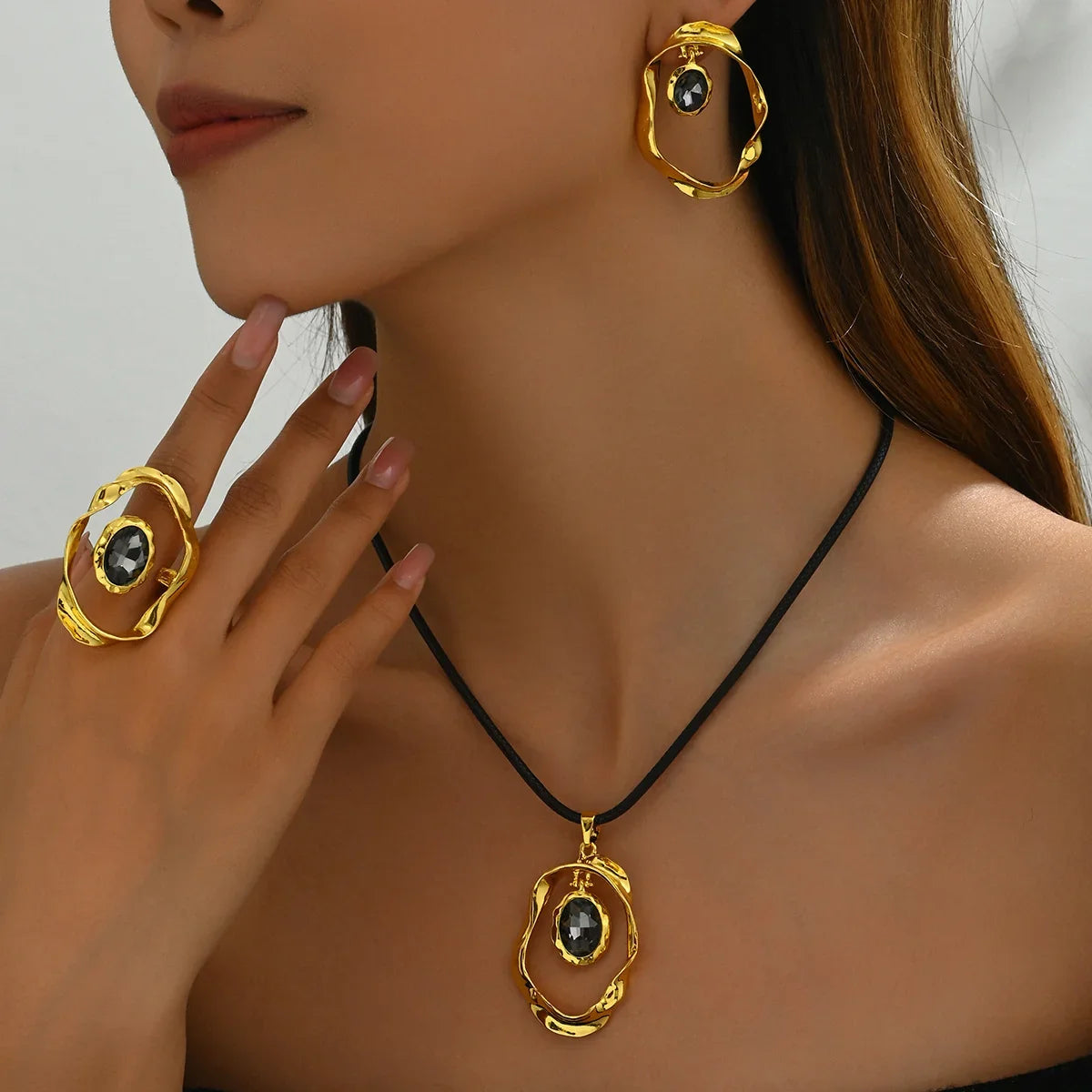 Woman wearing gold hoop earrings, a gold ring, and a gold pendant necklace with black stones.